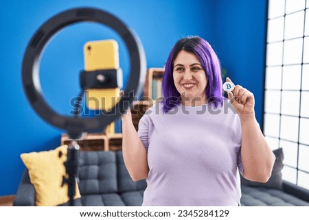 Plus size woman wit purple hair recording bitcoin tutorial with smartphone at home screaming proud, celebrating victory and success very excited with raised arm 