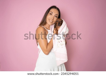 Young woman hugs her puppy Dachshund dog and looks at it. Love between dog and owner. Isolated on pink background. Studio portrait.