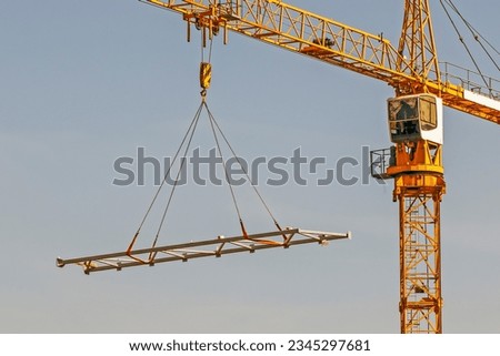 A construction crane lifts a metal structure on a summer day Royalty-Free Stock Photo #2345297681