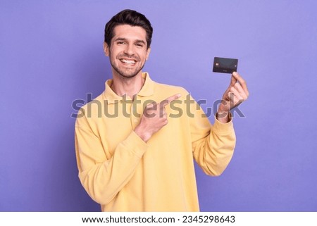 Photo of positive attractive guy beaming smile indicate finger arm hold debit card isolated on violet color background