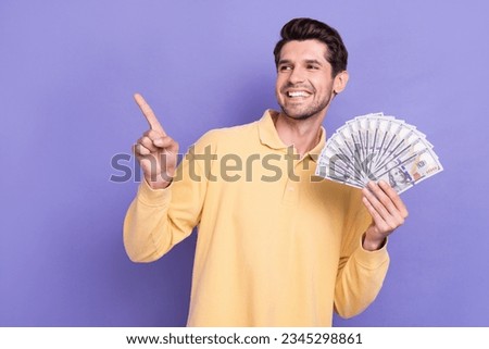Photo of cheerful person toothy smile hand hold dollar bills look direct finger empty space isolated on violet color background