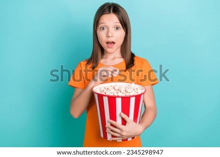 Photo of impressed speechless little girl wear orange stylish t-shirt eat popcorn astonished staring isolated on teal color background