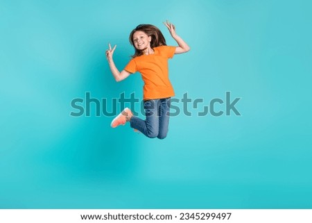 Photo of charming positive cute girl wear stylish orange clothes jump up v-sign good mood empty isolated on cyan color background