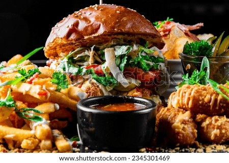 fast food set on plate. burger, potato chips, french fries, chicken wings, fried cheese and more on table.