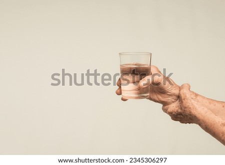 Close-up of hands senior woman trying to hold a glass of water. Causes of hand shaking include Parkinson's disease, stroke, or brain injury. Mental health neurological disorder Royalty-Free Stock Photo #2345306297
