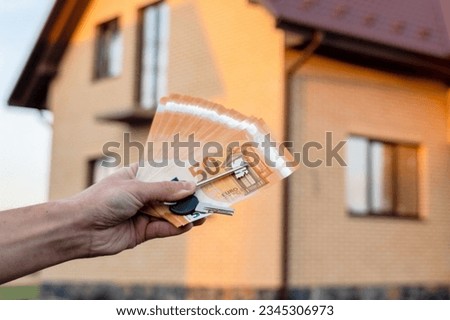 A Key and money in hands in front of home. Building, project, moving to new home, mortgage, rent and purchase real estate.