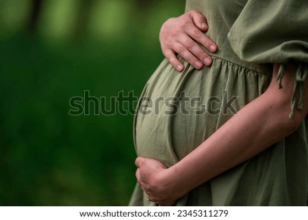 Caucasian Young Pregnant woman Tummy belly  summer green dress touching stomach field expecting a baby relaxing outside nature park lake rural Beautiful magic 8 months enjoying life glasses hat Royalty-Free Stock Photo #2345311279