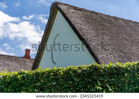 Triangular scandinavian danish thatched roof visible from behind the green hedge against the blue cloudy sky in the sunlight in Vejle, Denmark. Close up. Royalty-Free Stock Photo #2345325419