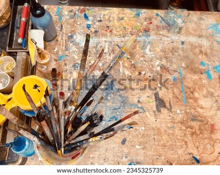 Top view of brushes and ink paint on top of wood table with random splash colourful ink splash around Royalty-Free Stock Photo #2345325739