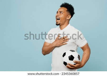 Side view young man fan wearing basic t-shirt sing national country anthem cheer up support football sport team hold in hand soccer ball watch tv live stream isolated on plain blue color background Royalty-Free Stock Photo #2345360857