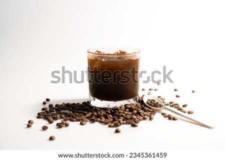 Image of iced black coffee in a glass, surrounded by coffee beans spilled on the floor.