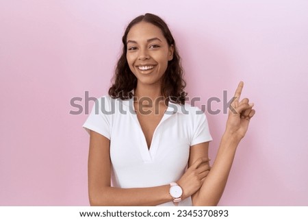 Young hispanic woman wearing casual white t shirt with a big smile on face, pointing with hand finger to the side looking at the camera. 