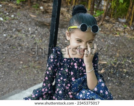 Rainy days, little girl wearing eyeglass and black dress. Standing on green grass. Portrait photo of seeing at sky.Comedy face style near footpath. 