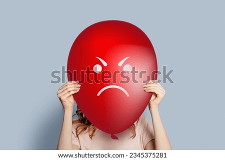 girl holding balloon with angry face isolated over grey background. Anger and annoyance concept