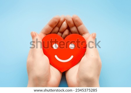 female hands hold a paper heart with happy smiley face isolated over blue background. broken help heart love concept