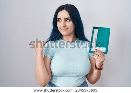 Young modern girl with blue hair holding l sign for new driver pointing thumb up to the side smiling happy with open mouth 