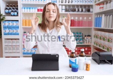 Young caucasian woman working at pharmacy drugstore using tablet relax and smiling with eyes closed doing meditation gesture with fingers. yoga concept. 