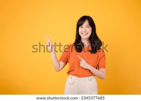 Experience happiness with a young Asian woman 30s, donning an orange shirt, pointing to free copy space on yellow background. recommending product concept.