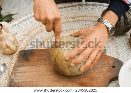 top view of unrecognizable male hands at home, cutting pumpkin to decorate halloween night on wooden board, concept of crafts, copy space.
