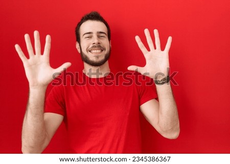 Young hispanic man wearing casual red t shirt showing and pointing up with fingers number ten while smiling confident and happy. 