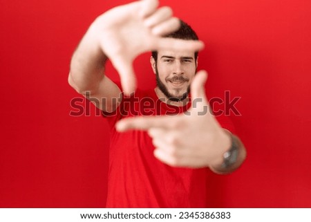 Young hispanic man wearing casual red t shirt smiling making frame with hands and fingers with happy face. creativity and photography concept. 