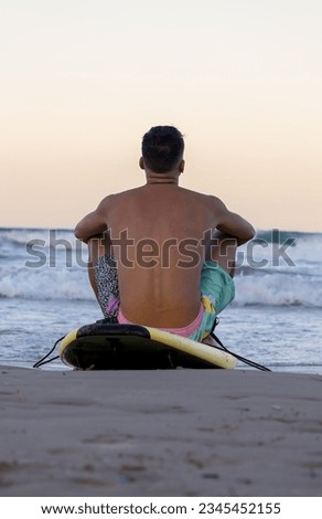 surfer sitting on the surfboard on the seashore