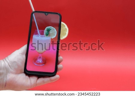 hand with a mobile phone photographing a fresh lemon juice