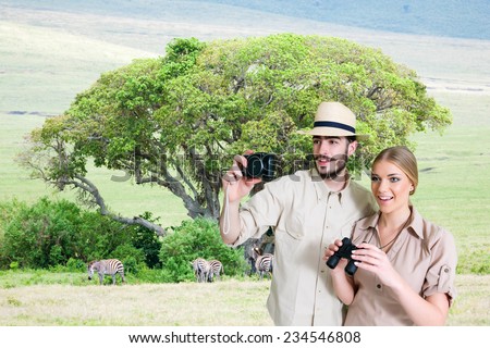 Young, happy couple taking a photo on the safari, Tanzania and Kenya.Acacia tree and animals in the background.Copy space
