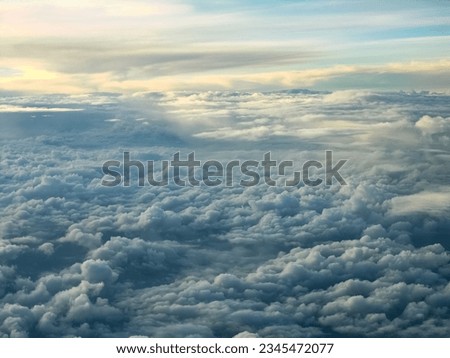 A stunning aerial view of clouds in the sky. The clouds are a variety of shapes and sizes, and they are arranged in layers. The sky is a deep blue, and there is a hint of sunlight peeking throug.