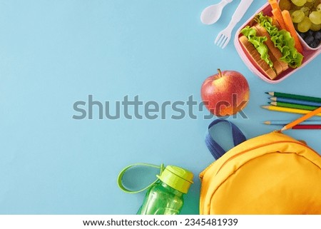 Appetizing and healthy school lunch concept. Top view flat lay of sandwiches, vibrant fruits and veggies, cutlery, bottle, school bag, pencils on light blue background with empty space for ads or text Royalty-Free Stock Photo #2345481939