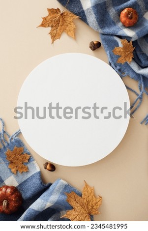 Embrace the fall coziness. Top view vertical photo of warm blanket, pumpkins, acorns, dry maple leaves on pastel beige background with blank circle for promo or text