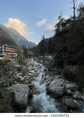 A fresh cold creek surrounded by trees with a building and mountains in the distance