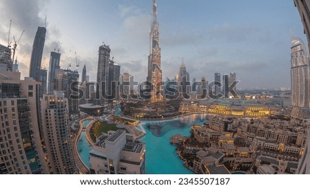 Skyscrapers rising above Dubai downtown day to night transition, mall and fountain surrounded by modern buildings aerial top panoramic view with cloudy sunset sky