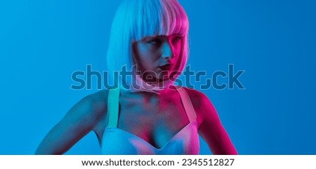Futuristic young female in wig looking to the side standing under neon light against blue background