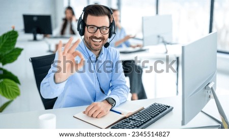 Male customer service representative showing approval sign to the camera, smiling and gesturing okay at call center office.