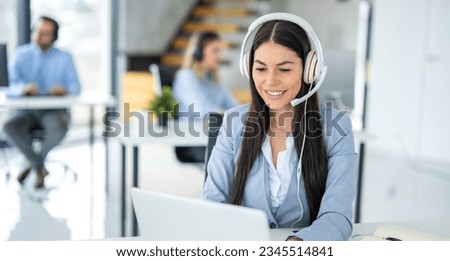 Portrait of friendly female customer support representative in headset with microphone consulting client while using laptop in customer support service office. Royalty-Free Stock Photo #2345514841