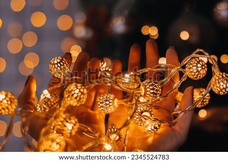 Female hands holding golden Christmas magic garland against a background of festive golden bokeh lights