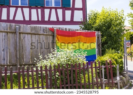 A large gay pride flag hanging on a wooden fence