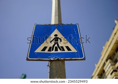 A low angle shot of a pedestrian crossing traffic sign on a blue sky background