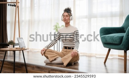 one woman adult caucasian female millennial using headphones for online guided meditation practicing mindfulness yoga with eyes closed on the floor at home real people self care concept copy space Royalty-Free Stock Photo #2345529593