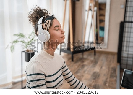 one woman adult caucasian female millennial using headphones for online guided meditation practicing mindfulness yoga with eyes closed on the floor at home real people self care concept copy space Royalty-Free Stock Photo #2345529619