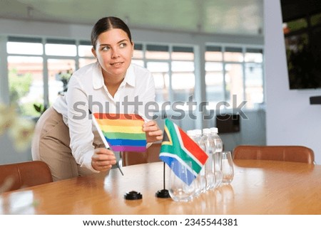 Preparing for business negotiations - woman sets small flags of countries of South Africa and LGBT on the table