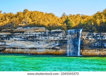 Waterfall cascading off Pictured Rocks cliff wall with multiple mineral colors painting the rocks