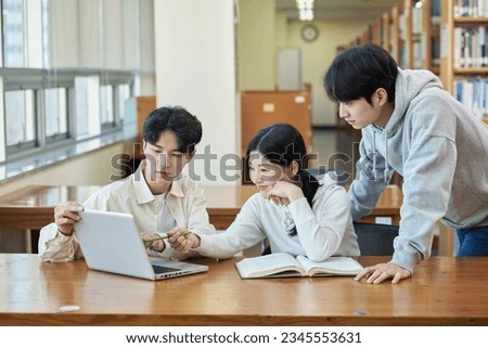 three young college student man and woman couple model and solo male model looking at laptop and book together in library of Asian Korean university Royalty-Free Stock Photo #2345553631