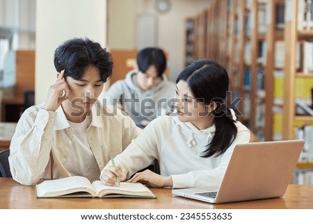 three young college student man and woman couple model and solo male model looking at laptop and book together in library of Asian Korean university