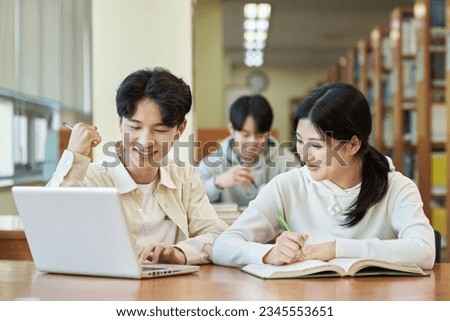 three young college student man and woman couple model and solo male model looking at laptop and book together in library of Asian Korean university Royalty-Free Stock Photo #2345553651