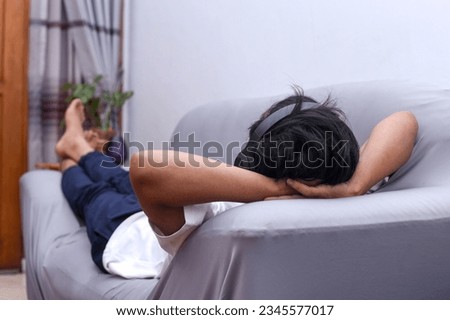 Full length view of Asian man with headphones laying on the sofa at home enjoying music