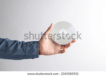 Man's hand in denim shirt holding white CD disk on gray background