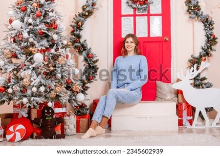 A young woman sits on a porch next to a Christmas tree and gifts.