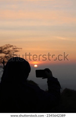Silhouette of Woman with Hijab Taking Picture of Sunrise in Wide Savannah